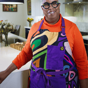 Woman wearing a multicolor abstract apron with purple straps from Black-owned brand soulPhoodie in a modern kitchen