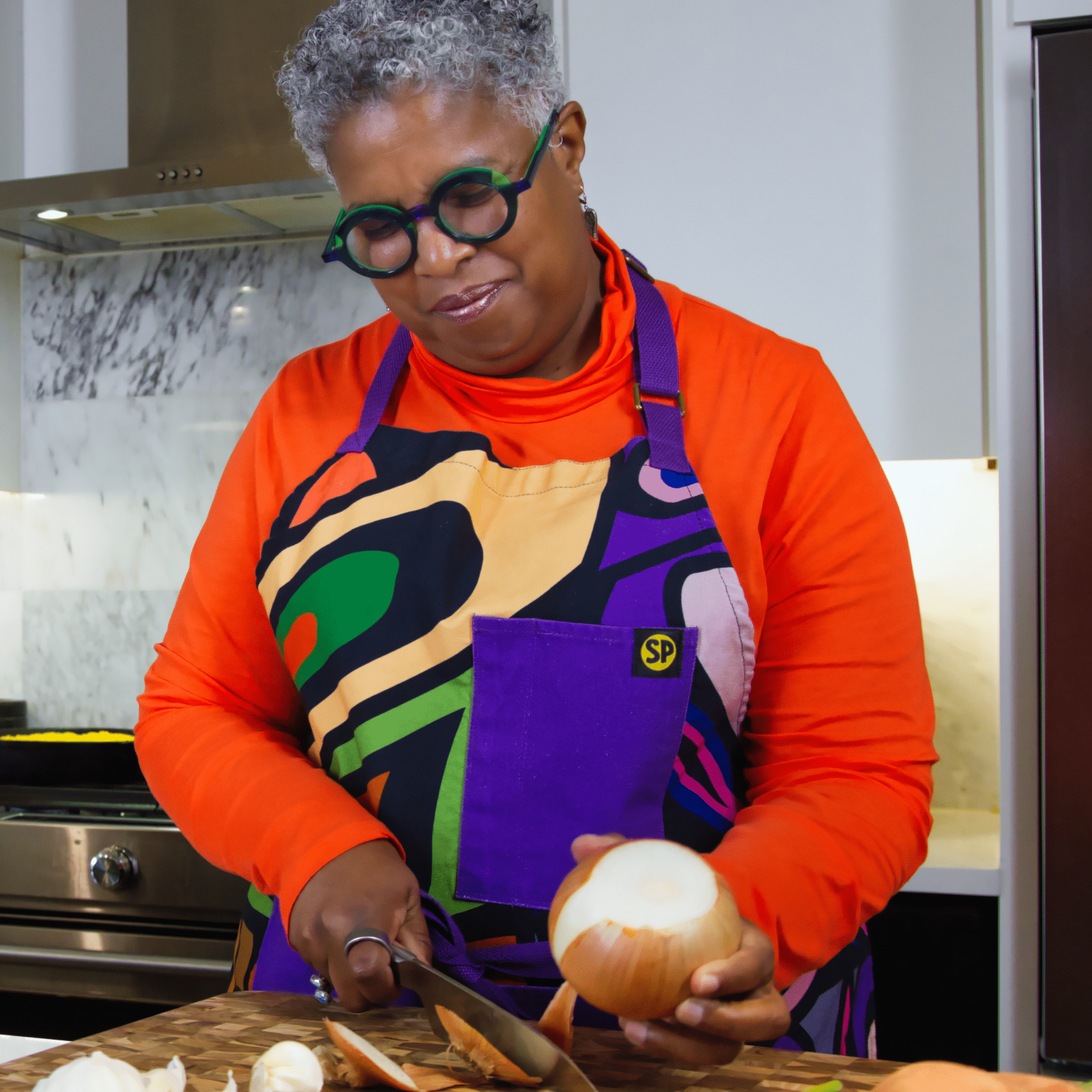 Woman wearing Beryl Apron with abstract multicolor design and purple pocket from Black-owned soulPhoodie chopping onions