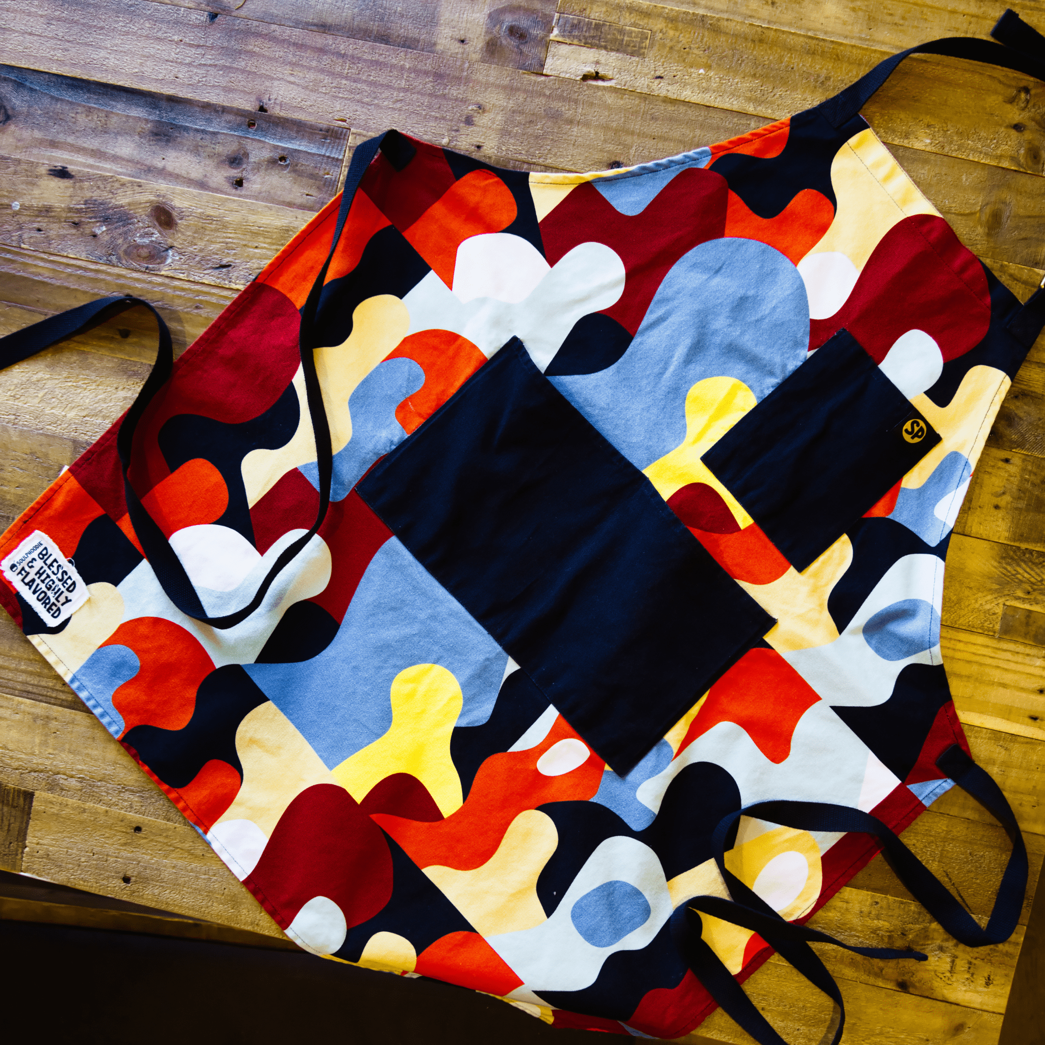 Beryl Apron with bold abstract multicolor pattern from Black-owned brand soulPhoodie on wood table