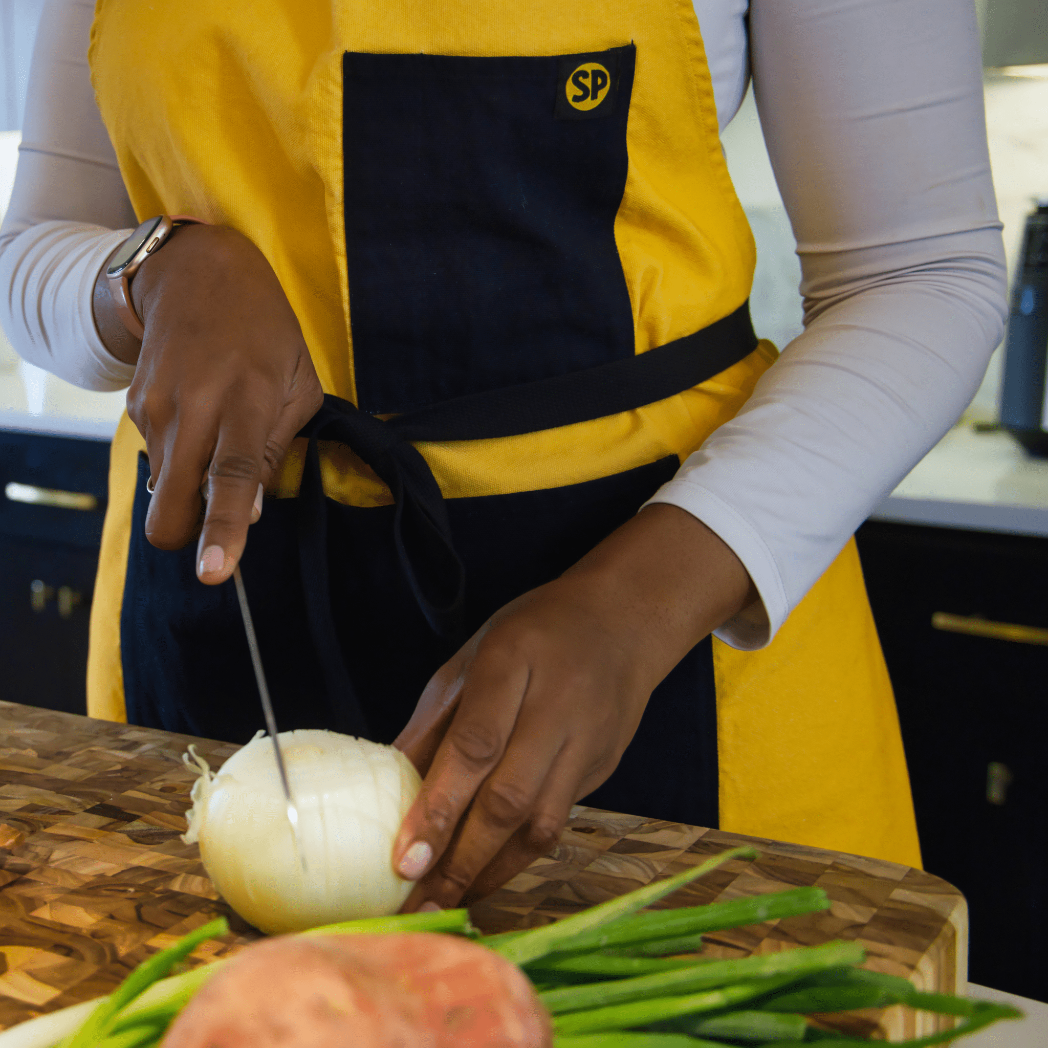 Close-up of cook slicing onion while wearing the Cornbread Gold Apron from Black-owned brand soulPhoodie in a modern kitchen.