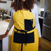 Woman wearing the Cornbread Gold Apron from Black-owned brand soulPhoodie with gold  and black pockets in a modern kitchen.