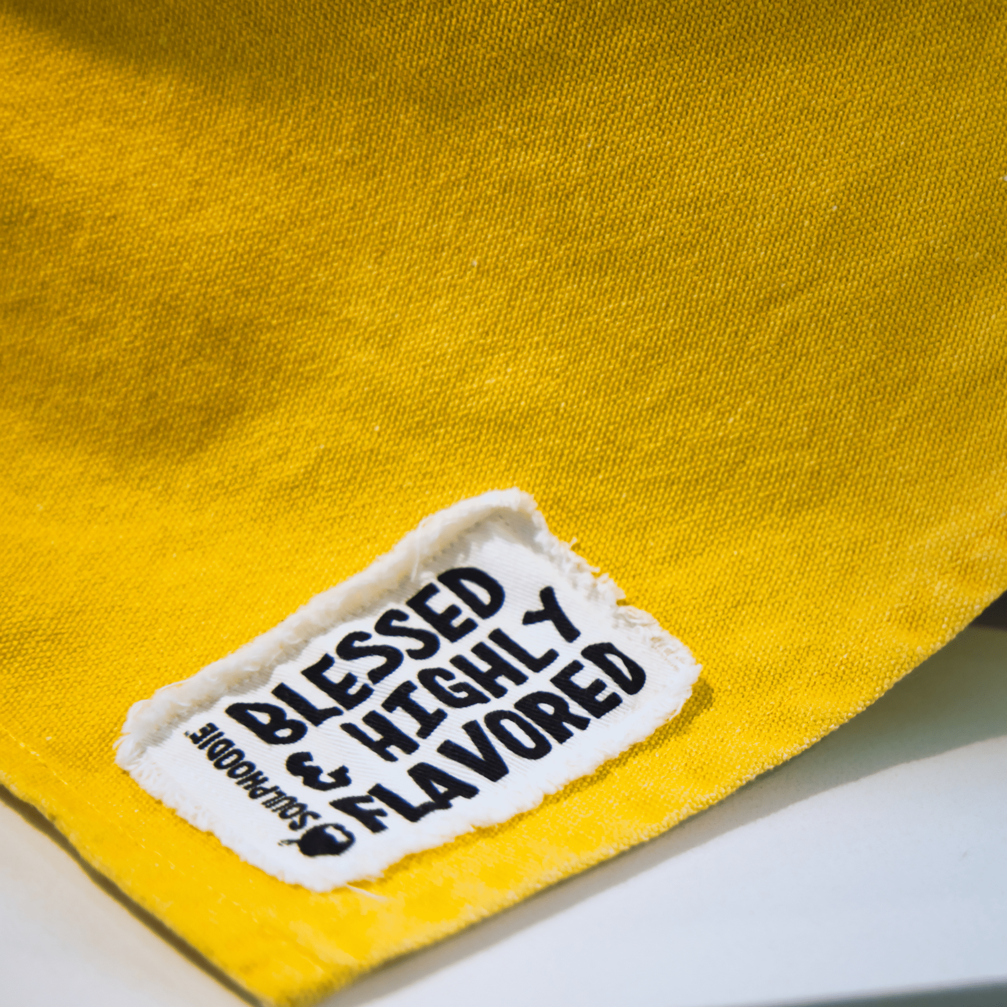Close-up of Blessed & Highly Flavored tag stitched on the Cornbread Gold Apron from Black-owned brand soulPhoodie.