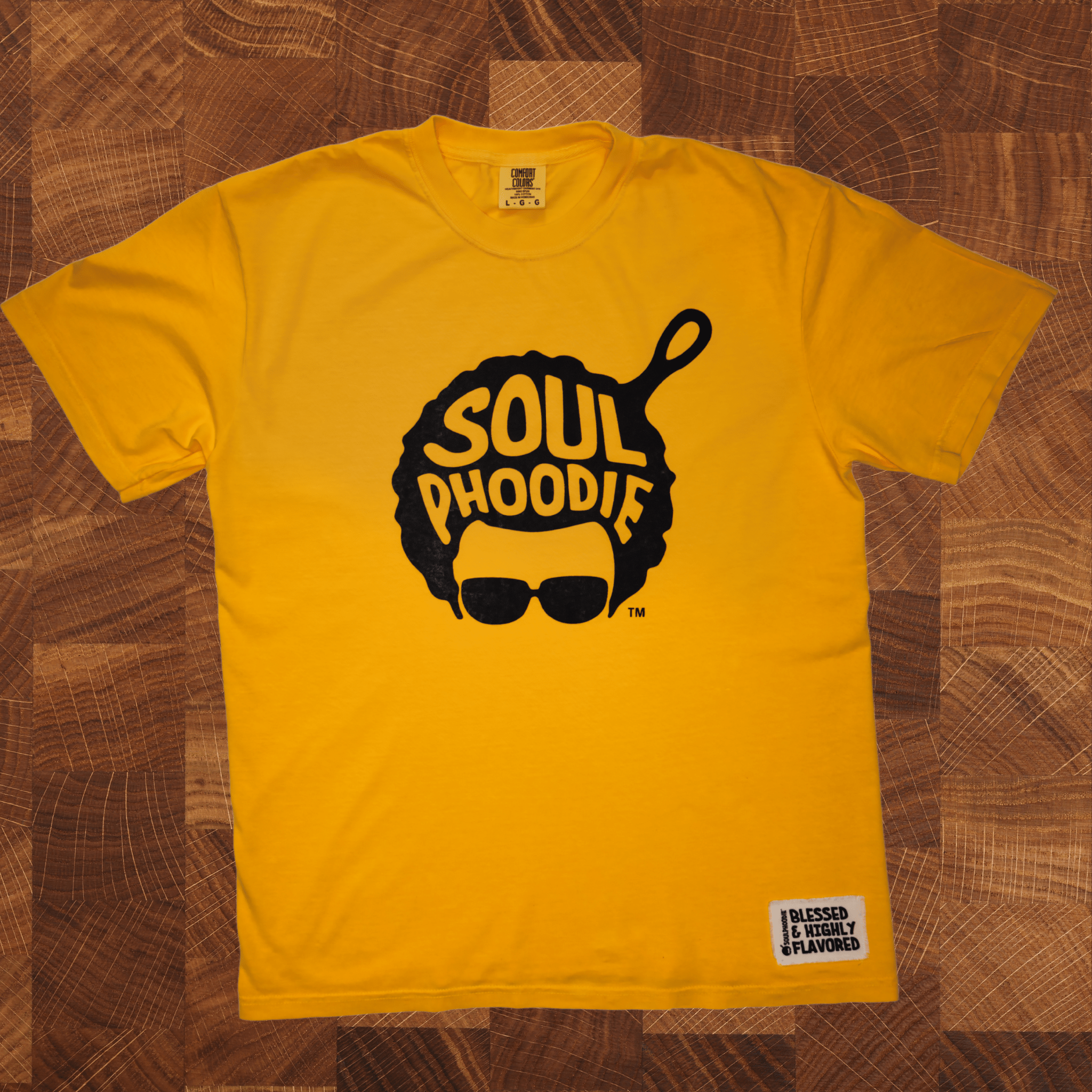 Yellow soulPhoodie Logo T-Shirt with skillet afro design displayed on wooden background.