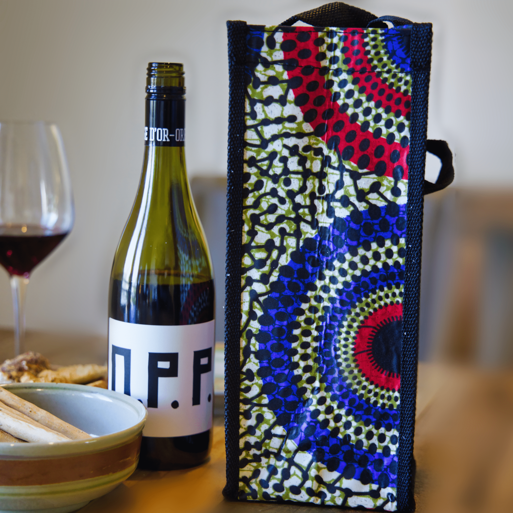 Colorful soulPhoodie wine bag with blue, red, and yellow circular design beside a bottle of wine on a wooden table.