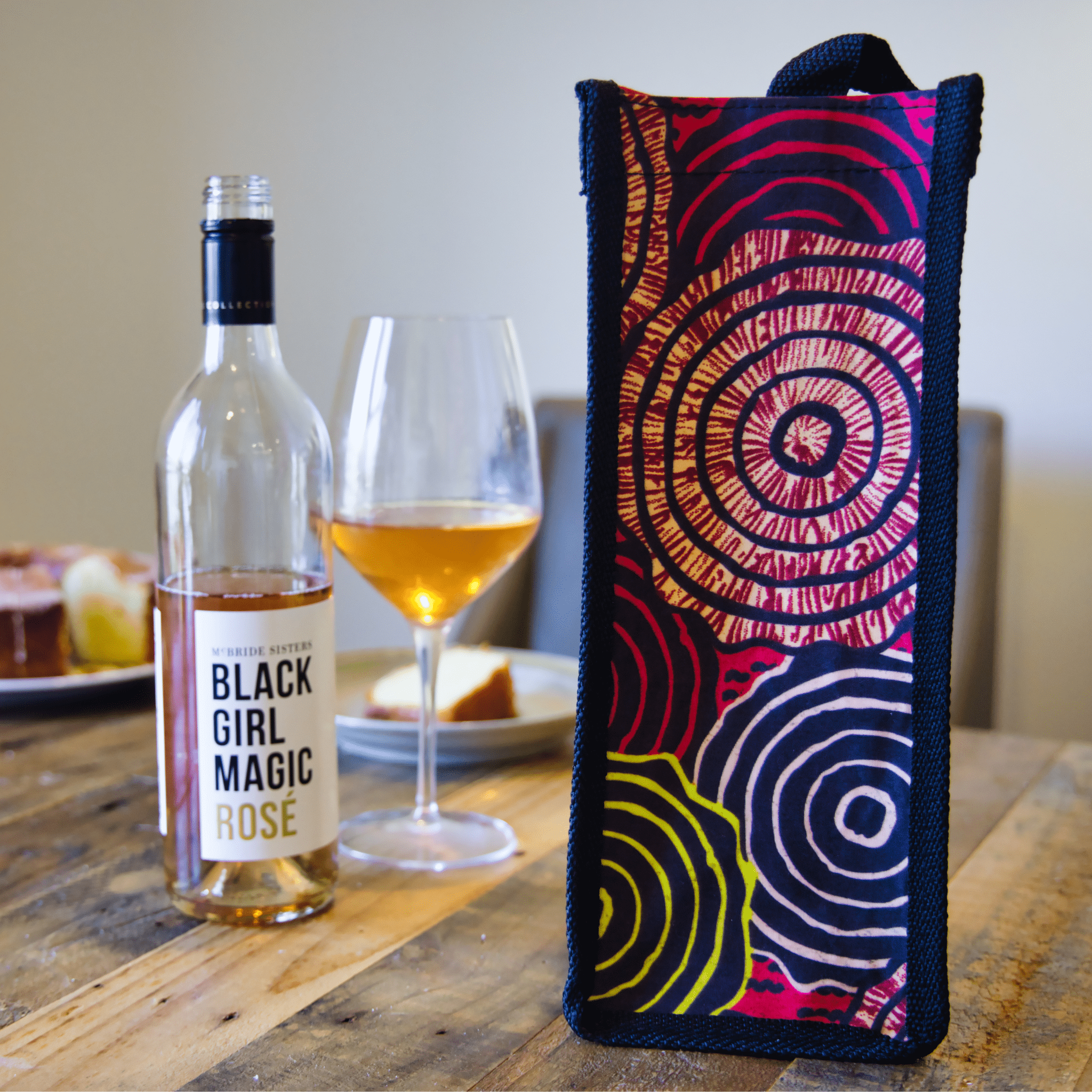 soulPhoodie wine bag with bold concentric patterns beside a glass of rosé and a bottle of Black Girl Magic wine.