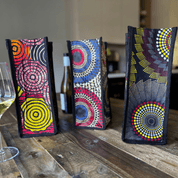 Three African-inspired wine bags from soulPhoodie featuring bold circular patterns and rich colors on a rustic wooden table