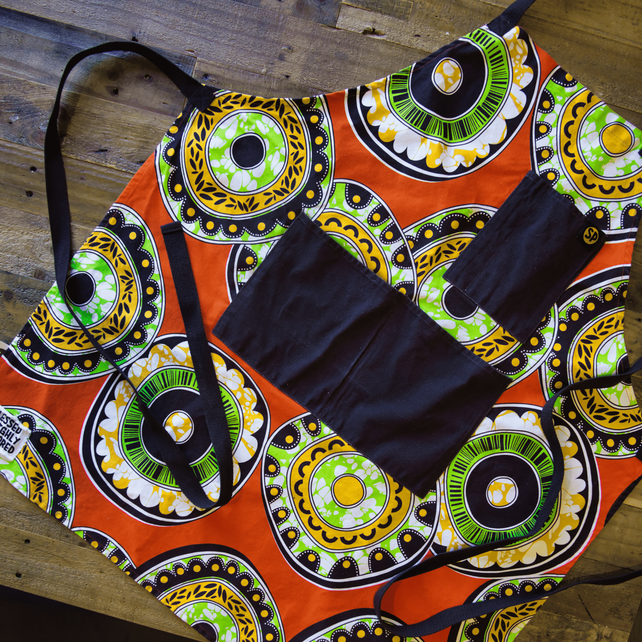 Flat lay of the Susan Apron from Black-owned brand soulPhoodie with bold orange, green, and yellow prints and brown pockets.