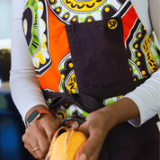 The Susan Apron from Black-owned brand soulPhoodie featuring bold orange, green, and yellow prints with brown pockets.