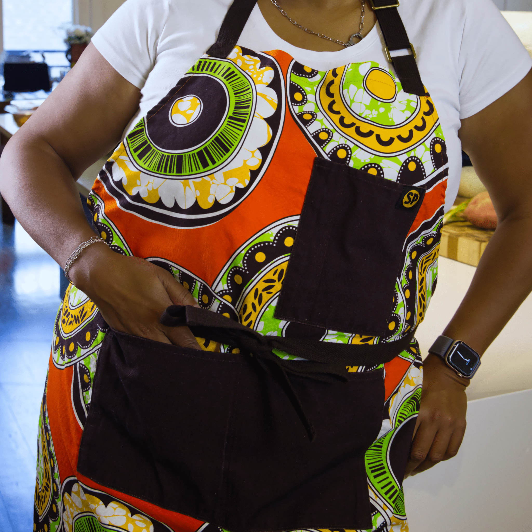 Woman wearing the Susan Apron from Black-owned brand soulPhoodie featuring bright orange, green, and yellow patterns.